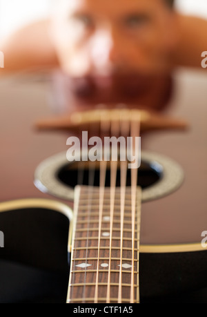 Macro shot down the fretboard of acoustic guitar with shallow depth of field with guitarist face in the distance reflected Stock Photo