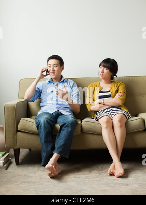 USA, Utah, Salt Lake City, Young couple sitting on sofa, man talking via mobile Stock Photo