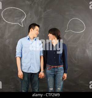 Young couple with speech bubbles on chalkboard, studio shot Stock Photo
