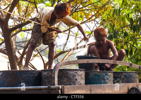 Young boys gathering fuel from the bottom of barrels near Mandalay, Myanmar Stock Photo