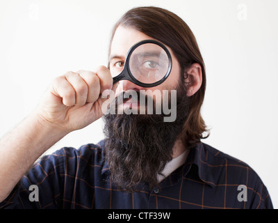 Bearded young man looking through magnifying glass Stock Photo