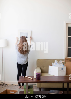 USA, Utah, Salt Lake City, Young woman hanging picture on freshly painted wall Stock Photo