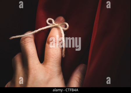 String tied around finger with deep red background Stock Photo