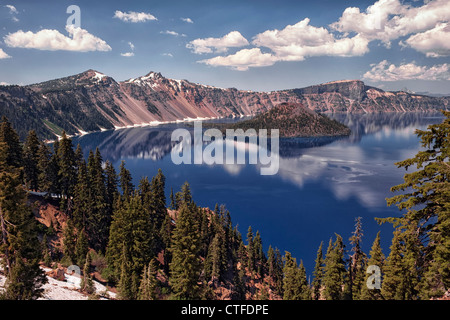 Afternoon clouds and Wizard Island reflect in the calm water of Oregon’s Crater Lake National Park. Stock Photo