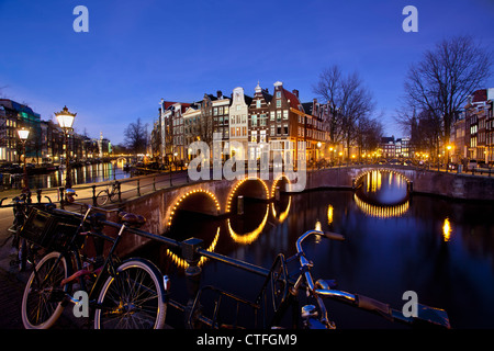 Amsterdam, Dusk, crossing of canals called Keizersgracht en Leidsegracht. Lit bridges, bikes. UNESCO World heritage Site.