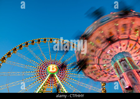 People on a chain swing ride at an amusement park with a ferris wheel in the background, Muenster, Germany. Stock Photo