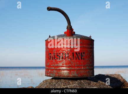 An old red gasoline can with spout sitting on a rock. Stock Photo