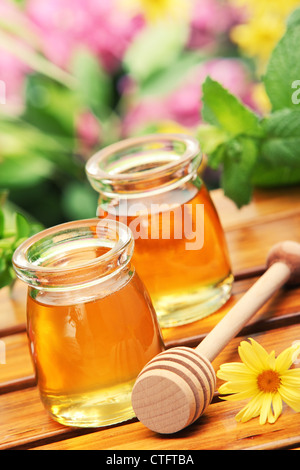 Honey in glass jars with flowers background. Stock Photo