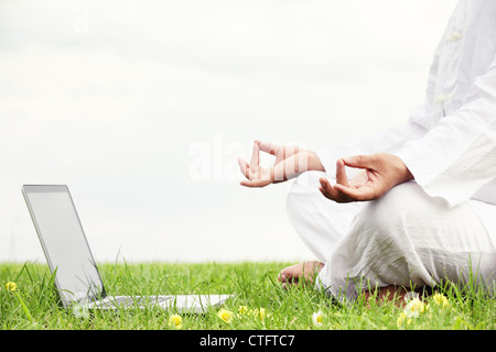 Man sitting in meditative lotus position with notebook on meadow. Stock Photo