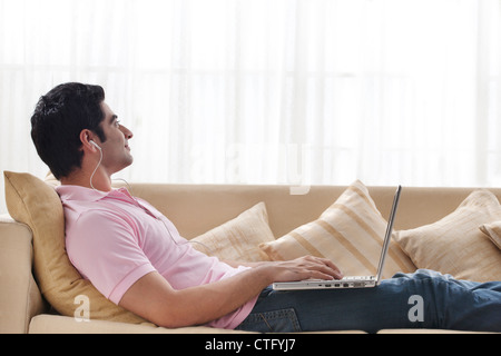 Young man contemplating while listening to music with laptop Stock Photo