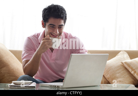 Smiling young man using laptop while having a cup of coffee Stock Photo