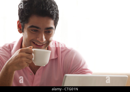 Smiling man having coffee while using laptop Stock Photo