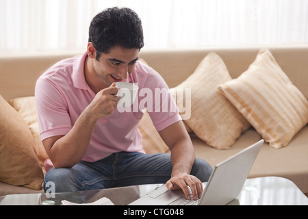 Happy man sipping coffee while using laptop at home Stock Photo