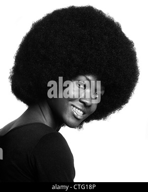 1970s PORTRAIT OF SMILING AFRICAN AMERICAN WOMAN WITH LARGE AFRO HAIR STYLE LEANING FORWARD LOOKING AT CAMERA OVER SHOULDER Stock Photo