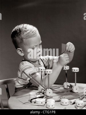 1960s BOY SEATED AT TABLE PLAYING WITH TINKER TOY CONSTRUCTION SET Stock Photo