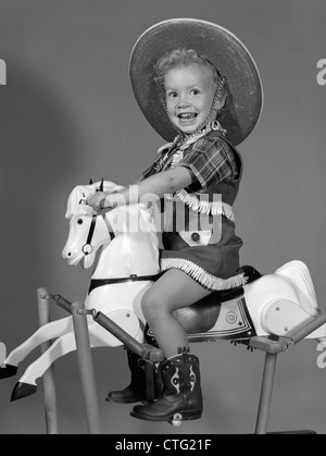 1950s GIRL DRESSED AS COWGIRL RIDING ROCKING HORSE Stock Photo