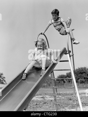 1940s GIRL GOING DOWN SLIDE BOY WAITING AT TOP Stock Photo