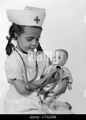 1960s GIRL IN NURSE UNIFORM HOLDING STETHOSCOPE TO BABY DOLL CHEST INDOOR Stock Photo