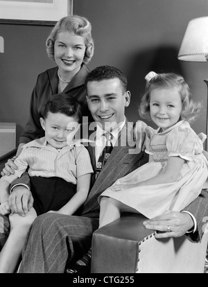 1940s 1950s FAMILY OF FOUR PORTRAIT SITTING IN LIVING ROOM CHAIR LOOKING AT CAMERA Stock Photo