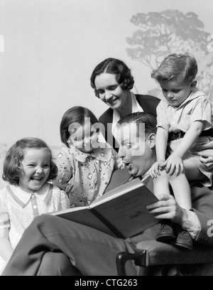 1930s FAMILY OF FIVE GROUPED AROUND FATHER READING CHILDREN'S PUNCH BOOK Stock Photo