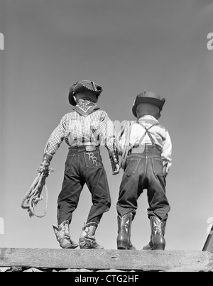 1950s BACK VIEW OF TWO BOYS DRESSED IN COWBOY COSTUME Stock Photo