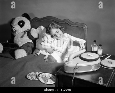 1950s SICK LITTLE GIRL IN BED PLAYING WITH RECORD PLAYER Stock Photo