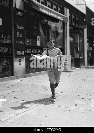 1930s NEWSPAPER BOY IN KNICKERS WALKING TOWARDS CAMERA ON STREET HOLDING PHILADELPHIA INQUIRER Stock Photo