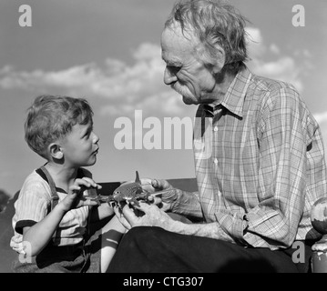 1940s BOY LOOKING AT MODEL PROPELLER PLANE WITH GRANDFATHER