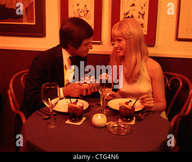 1970s MAN GIVING WOMAN PRESENT AT RESTAURANT TABLE Stock Photo