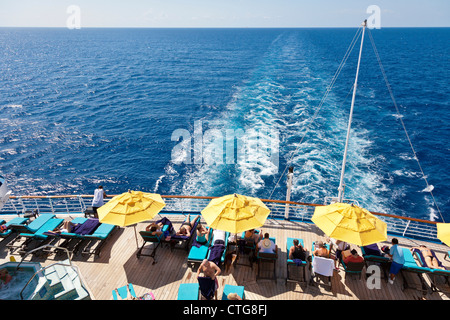 Sunbathing cruise passengers watch wake behind stern of Carnival Fascination cruise ship Stock Photo