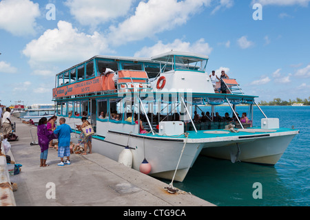 Four black people shop for starfishes and shells next to snorkeling excursion boat at dock in Nassau, Bahamas Stock Photo