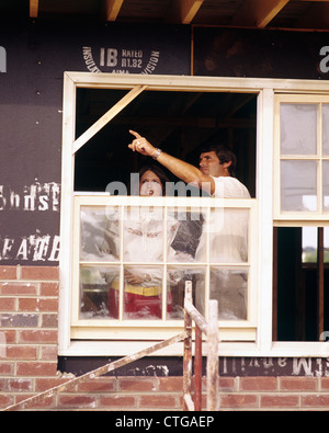 1970s COUPLE MAN WOMAN IN HOUSE UNDER CONSTRUCTION MAN POINTING OUT OF WINDOW Stock Photo