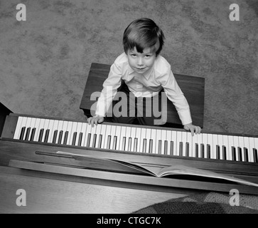 1980s OVERHEAD OF BOY SITTING ON BENCH WITH FINGERS ON PIANO KEYS LOOKING UP Stock Photo