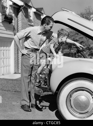 1940s FATHER & SON CHECKING UNDER HOOD OF CAR IN DRIVEWAY Stock Photo