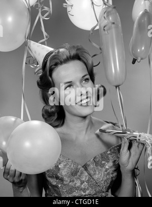 1960s 1950s WOMAN IN PARTY DRESS SMILING HOLDING BALLOON AND NOISE MAKER Stock Photo