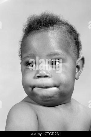 1960s PORTRAIT OF AFRICAN-AMERICAN BABY MAKING A FUNNY FACE BITING HIS LIP Stock Photo