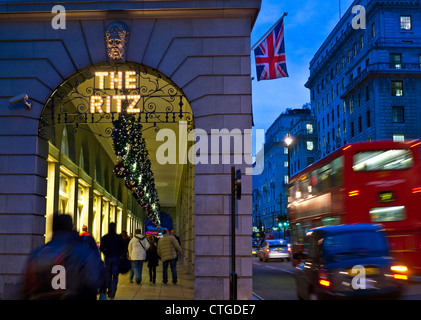 The Ritz Hotel at Christmas with Union Jack flag shoppers and passing red buse and black taxi cab Piccadilly London UK Stock Photo