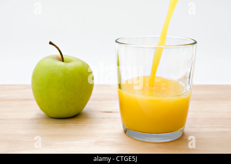 Glass of orange juice being poured and green apple on wooden chopping board against a white background Stock Photo