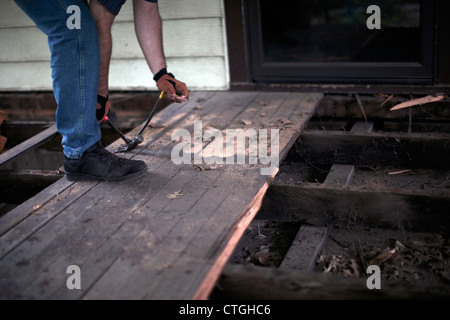Man using hammer and prybar to remove porch decking planks. Stock Photo