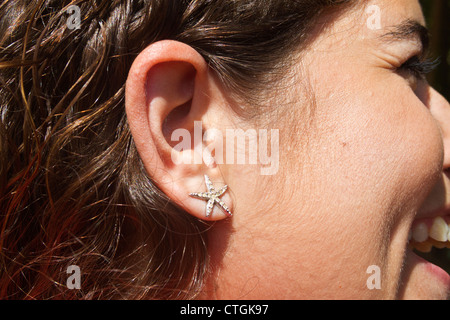 Star shaped earring on smiling young woman's ear. Stock Photo