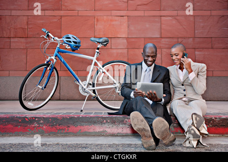 Business people sitting on curb using digital tablet and cell phone Stock Photo
