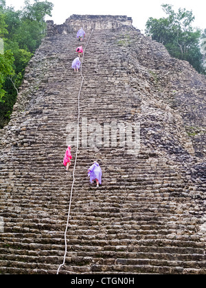 Visitors in raincoats climb Nohoch Muul, a Maya temple at Coba, Mexico Stock Photo