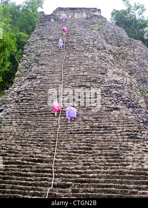 Visitors in raincoats climb Nohoch Muul, a Maya temple at Coba, Mexico Stock Photo