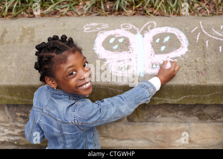 Mixed race girl drawing on cement with chalk Stock Photo