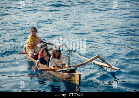 Indonesian children in a dugout outrigger canoe paddle up to seil pearls to tourists anchored off of Komodo Island, Indonesia. Stock Photo