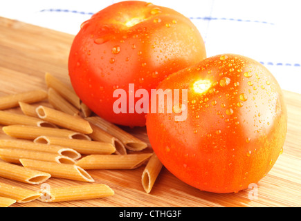Red ripe tomatoes with whole grain pasta on wooden cutting board. Stock Photo