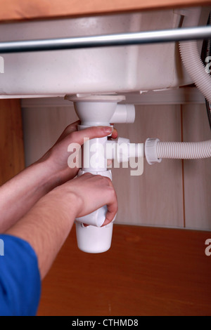 Plumber fitting the waste pipe to a kitchen sink Stock Photo