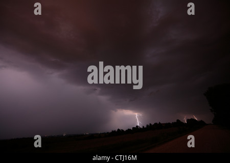 Lightning strikes far away during a night thunderstorm, with heavy rain falling on the left side of the image. Stock Photo