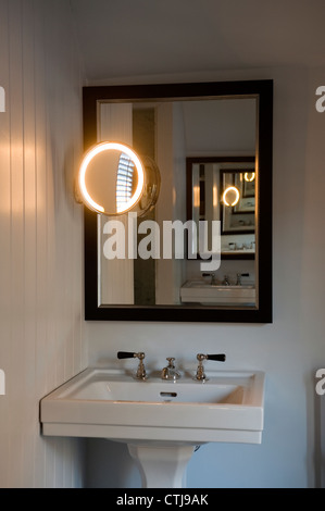 Hand basin with nickle taps and nickle circular lit mirror Stock Photo