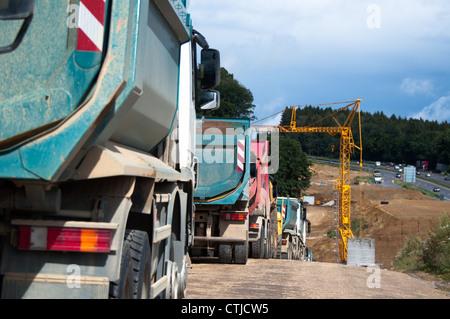 Row of dum trucks being parked at a highway construction site in Germany Stock Photo